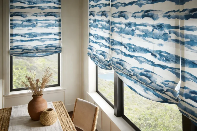 Dining room with blue pattern Roman shades on windows, a wicker table with a vase, and a view outside.