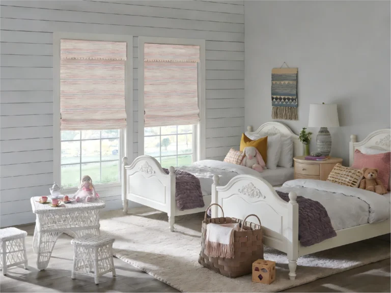 Kids' bedroom featuring two white wooden twin beds with plush toys, wicker furniture, and decorative window shades.