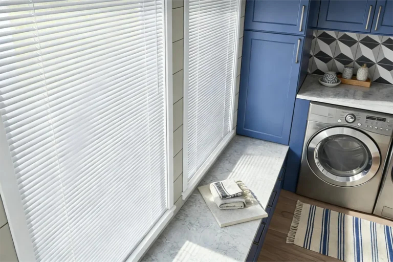 Laundry room featuring blue cabinets, geometric backsplash, a stainless steel dryer, white blinds, and a striped rug on wood floor.
