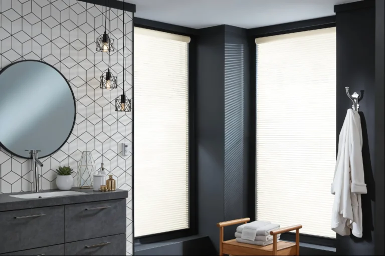 Bathroom interior featuring geometric wall tiles, circular mirror, hanging lights, dark drawers, robes, and towels near large windows.