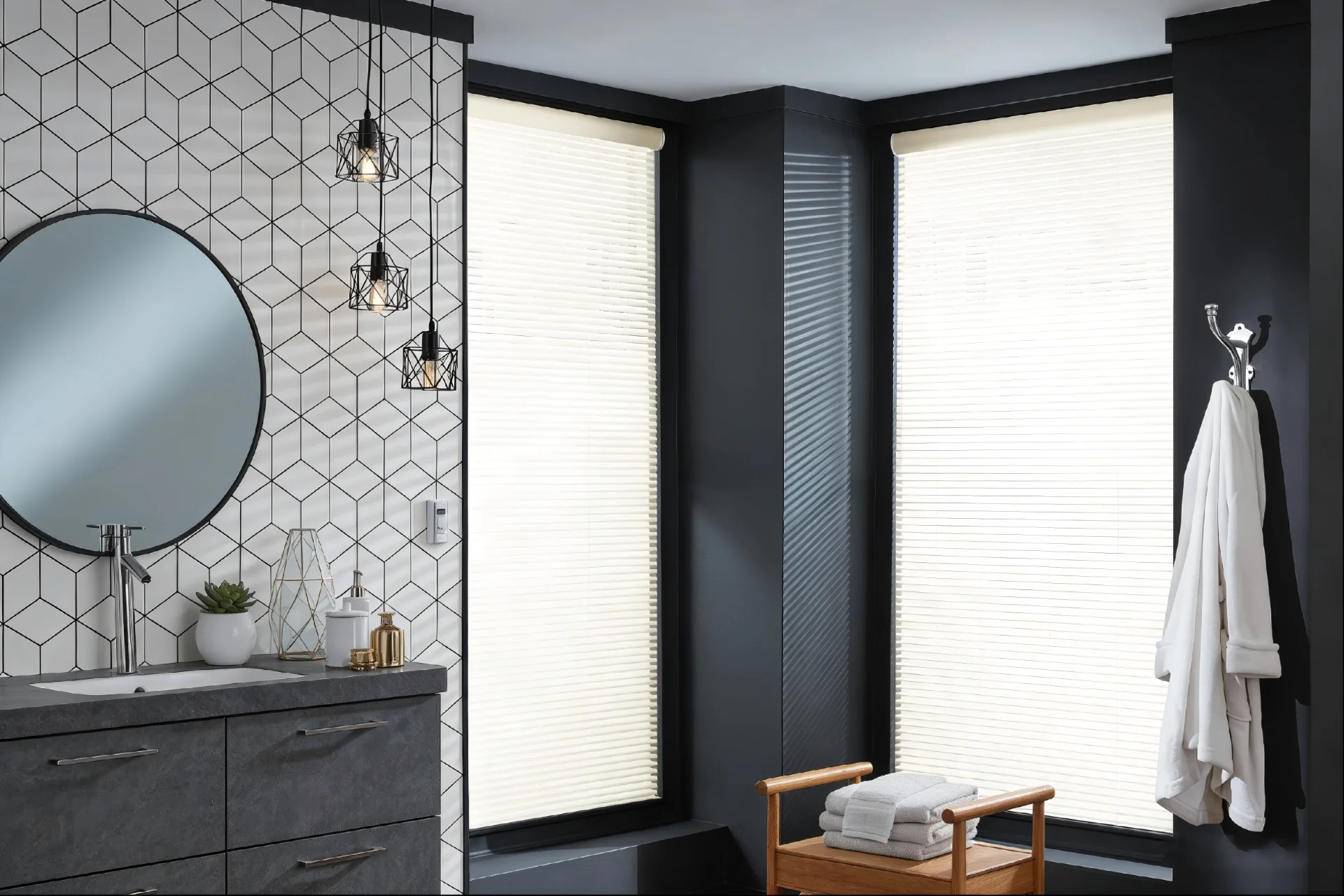 Bathroom interior featuring geometric wall tiles, circular mirror, hanging lights, dark drawers, robes, and towels near large windows.