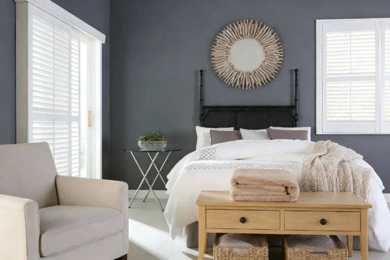 Contemporary bedroom featuring gray walls, white bedding with pillows, a round mirror, and light wood furniture for a cozy atmosphere.