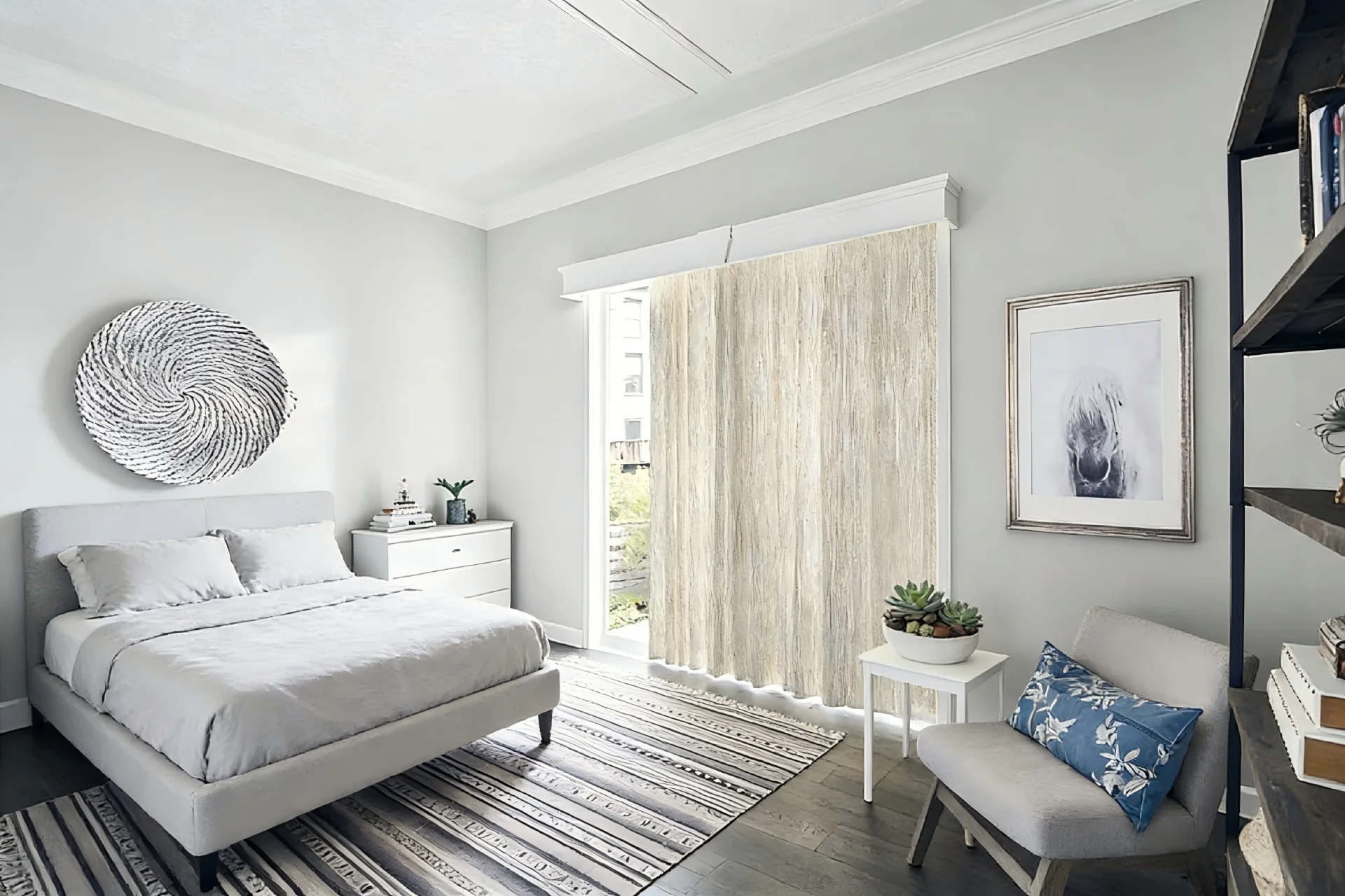 Modern bedroom with a neutral color scheme, featuring a bed, white dresser, large decorative wall piece, artwork, and a cozy chair with a blue cushion.