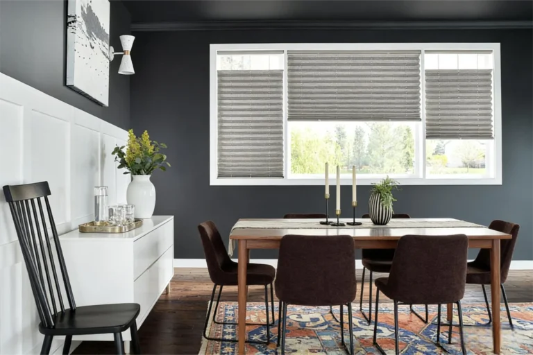 Dining room with dark walls, wooden table, dark chairs, a patterned rug, and a white sideboard with a vase and glasses.