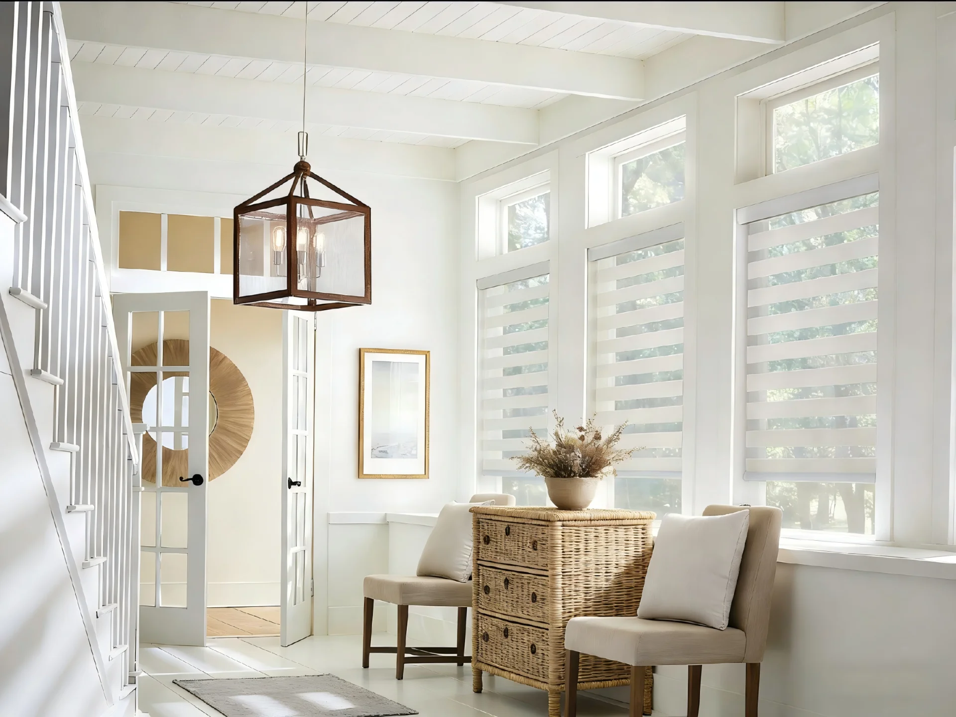 Bright entryway with striped blinds, wicker dresser, modern pendant light, two chairs, and wall art beside a staircase.