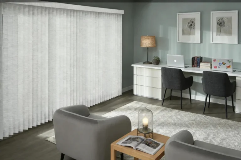 Modern home office featuring vertical blinds, gray chairs, a desk with laptops, a table lamp, and wall art.
