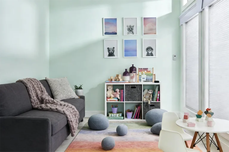 A modern playroom with a dark grey sofa and colorful cushions, abstract art on the walls, toys, and a white table with chairs.