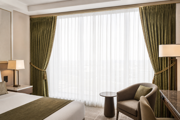 Layered hotel window treatment with closed white sheers and olive-green blackout curtains stacked at the sides