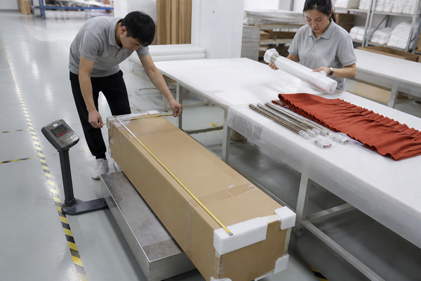 Factory workers measuring and weighing a long curtain carton