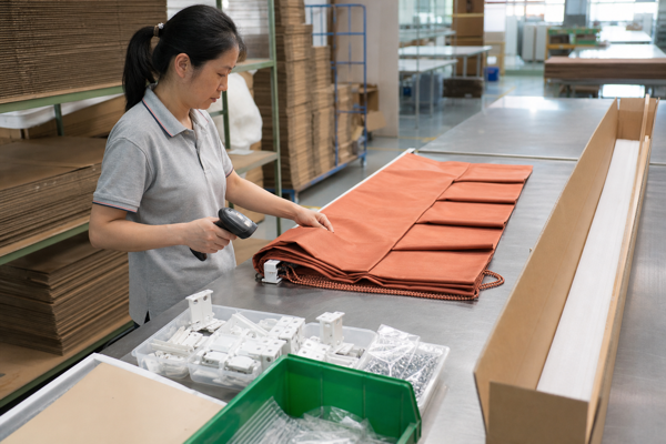Factory worker checking a terracotta Roman shade, accessories, and order label at a packing station