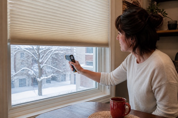 A homeowner checking the window area beside an ivory cellular shade on a snowy day
