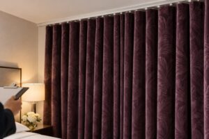 Closed aubergine hotel curtains hanging from a white ceiling track